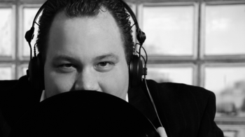 Foto: DJ DeeNoeRee mit Gesicht zur Hälfte hinter Mikrofon versteckt